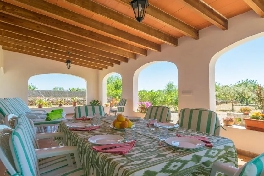 A covered outdoor dining area with a long table and striped seating.