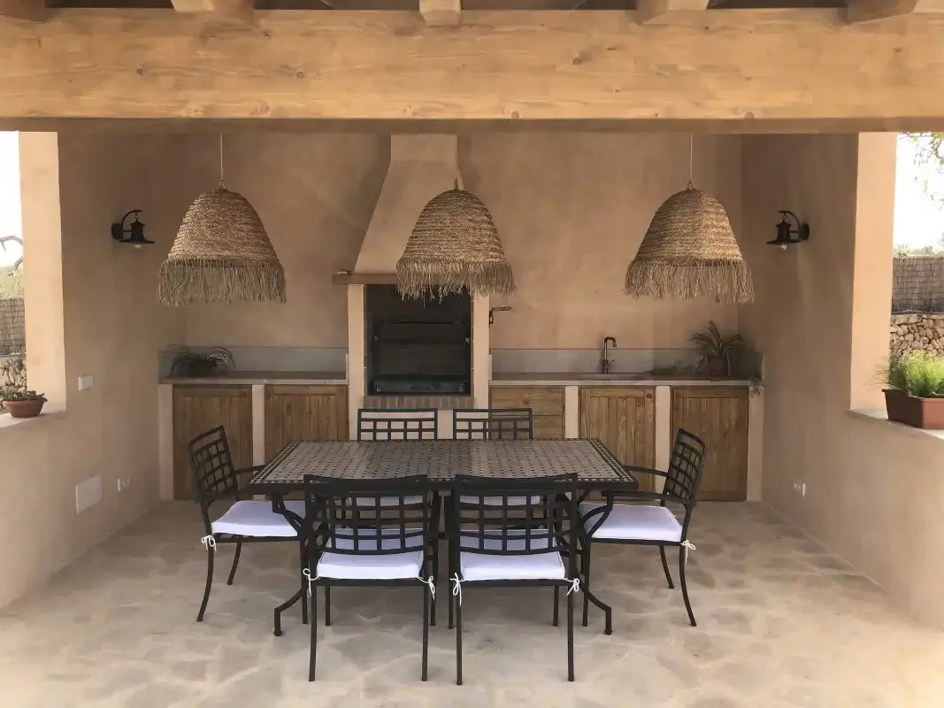Un comedor exterior cubierto tiene una mesa y sillas bajo lámparas colgantes de tejido.