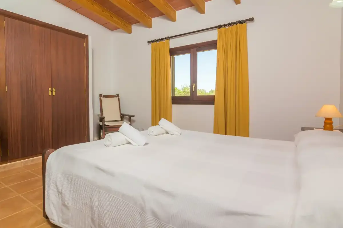 Un dormitorio con ropa de cama blanca, vigas de madera y cortinas amarillas.