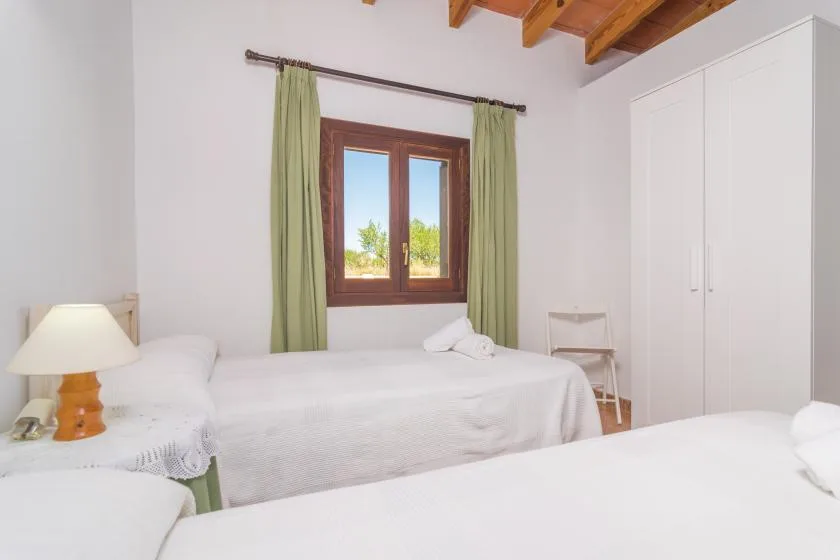 Un dormitorio luminoso con ropa de cama blanca, una ventana de madera y cortinas verdes.