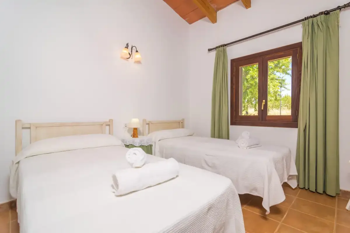 Un dormitorio con dos camas, ropa de cama blanca y una ventana con cortinas verdes.