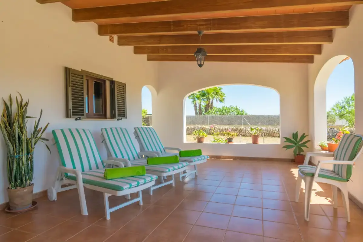 Un patio cubierto con asientos a rayas y arcos abiertos da a un jardín.