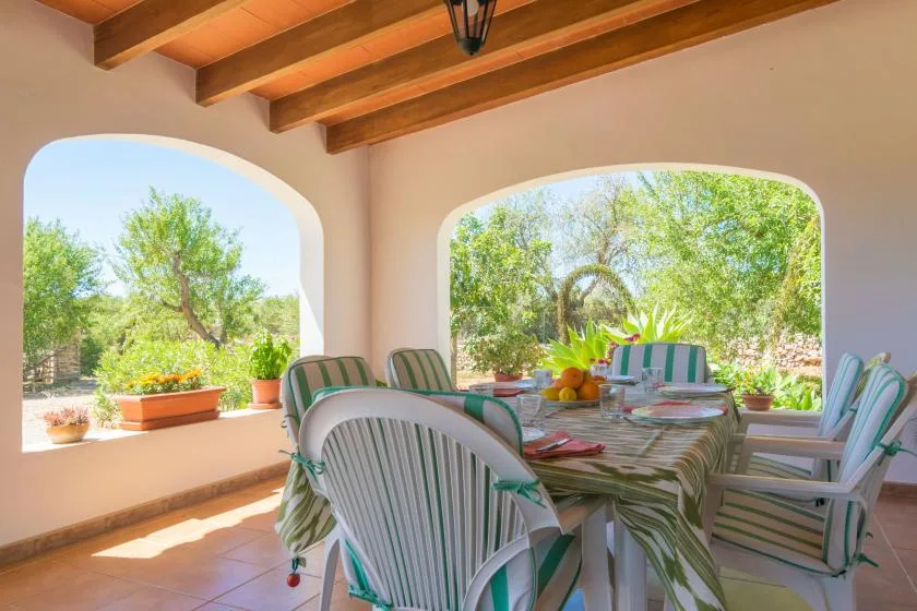 Un comedor en una terraza cubierta se abre a un jardín frondoso.