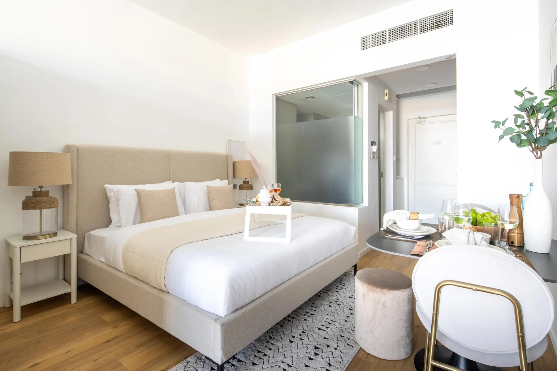 A bright bedroom with a neatly made bed and a small dining area.