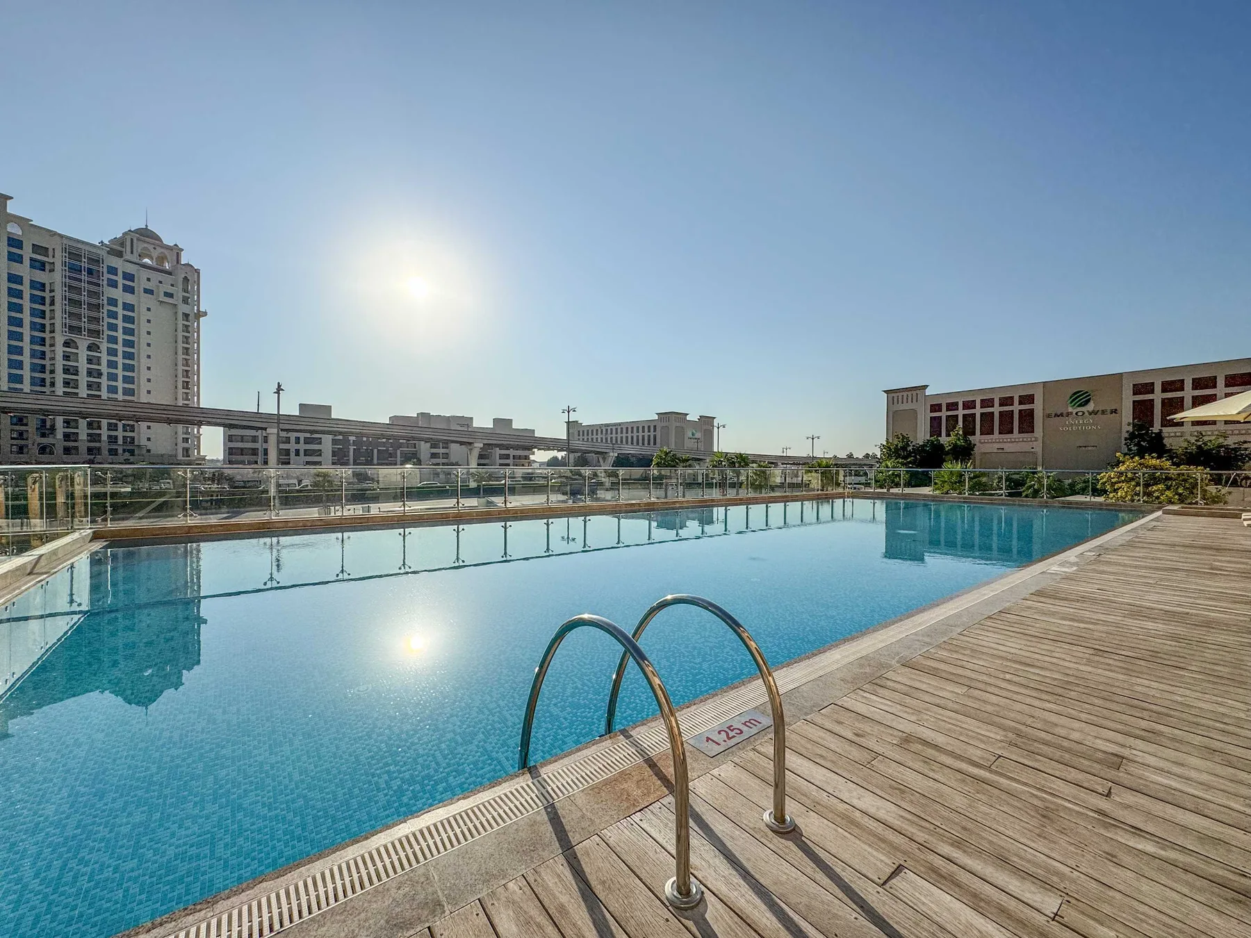 A large outdoor swimming pool beside a wooden deck, with buildings in the background.