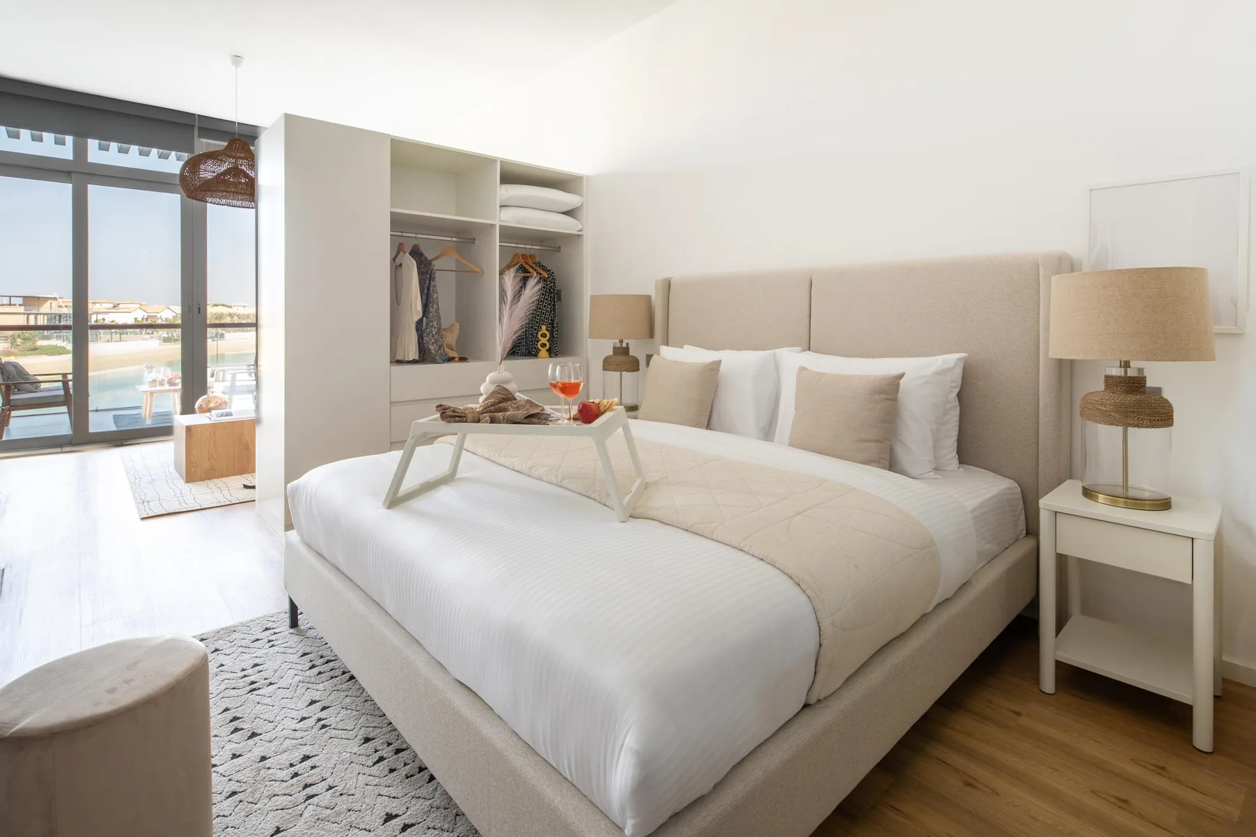 A bright bedroom with a large bed, bedside tables, and an open wardrobe.