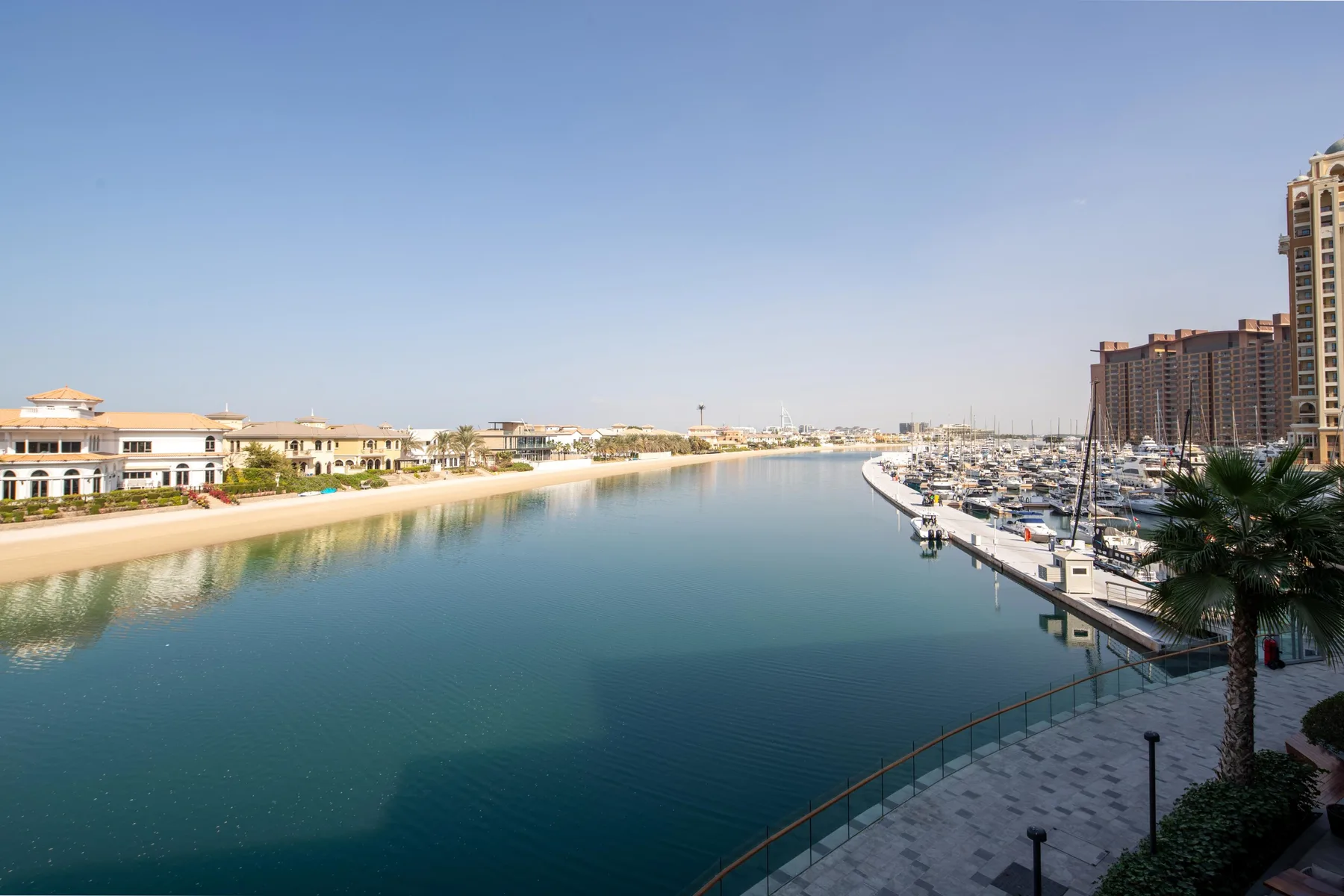 A marina lined with boats borders a calm waterway between waterfront buildings.