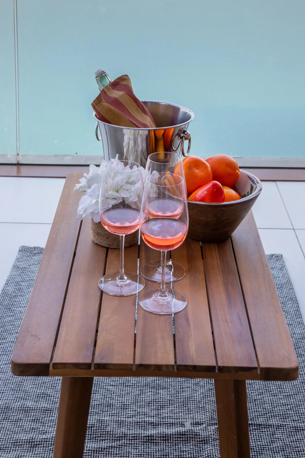 A low wooden table displays wine glasses, a chilled bottle, and a bowl of oranges.