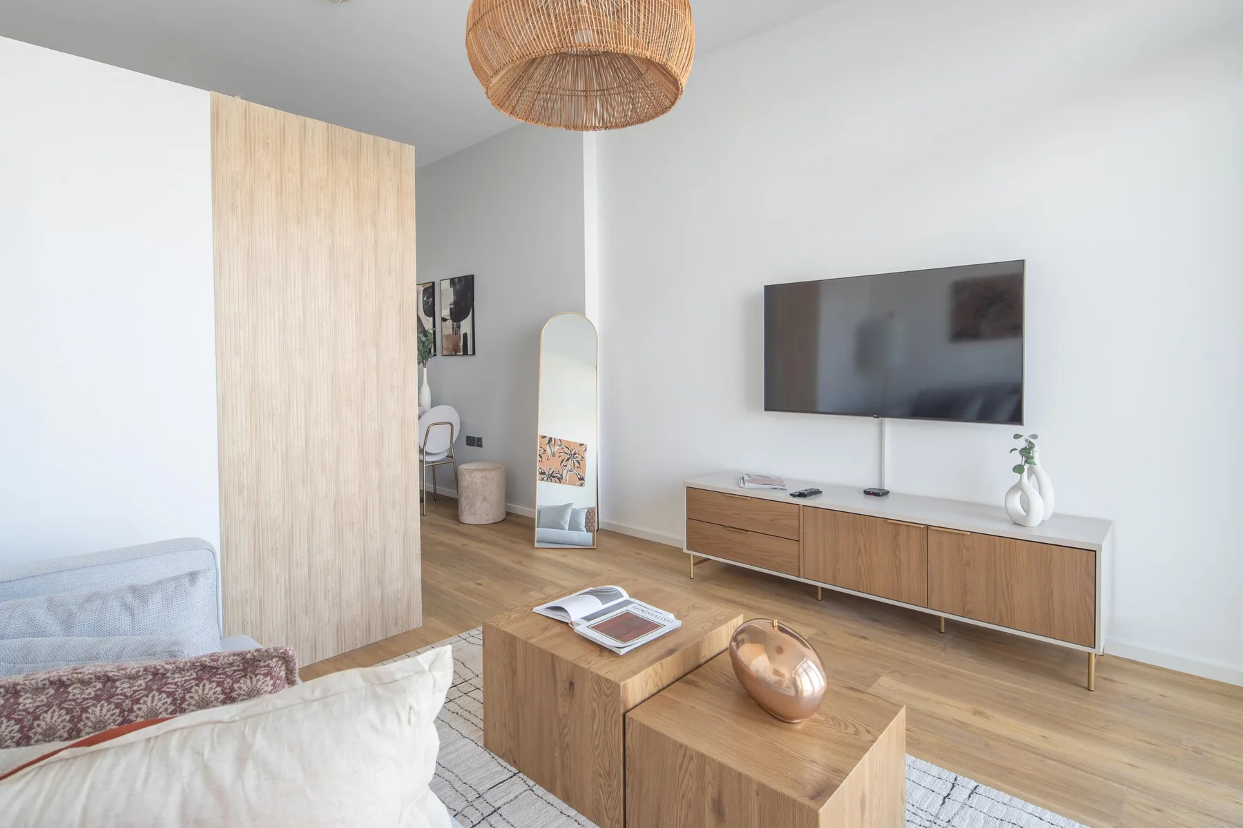 A bright living room with a wall-mounted television and wooden furniture.