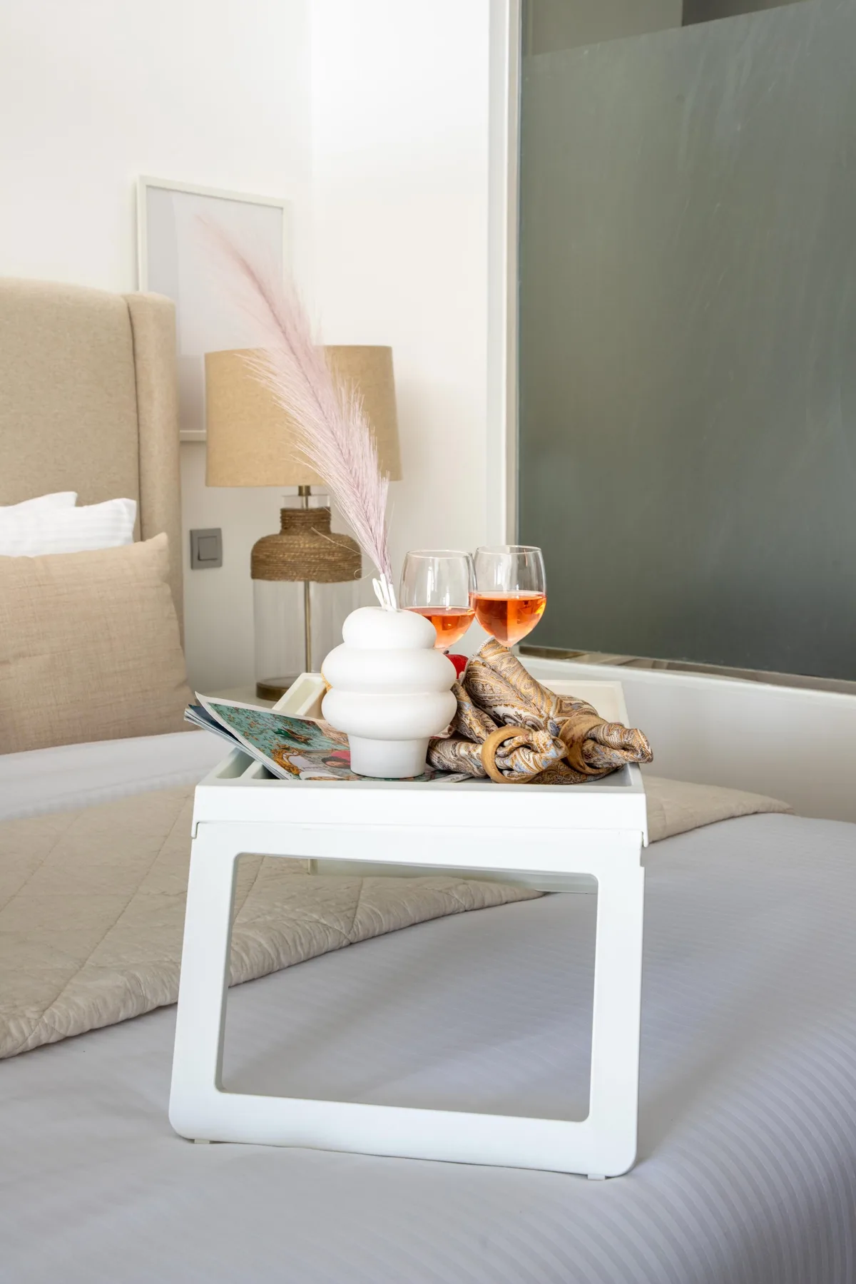 A bedroom scene with a white tray table displaying decor and two glasses.