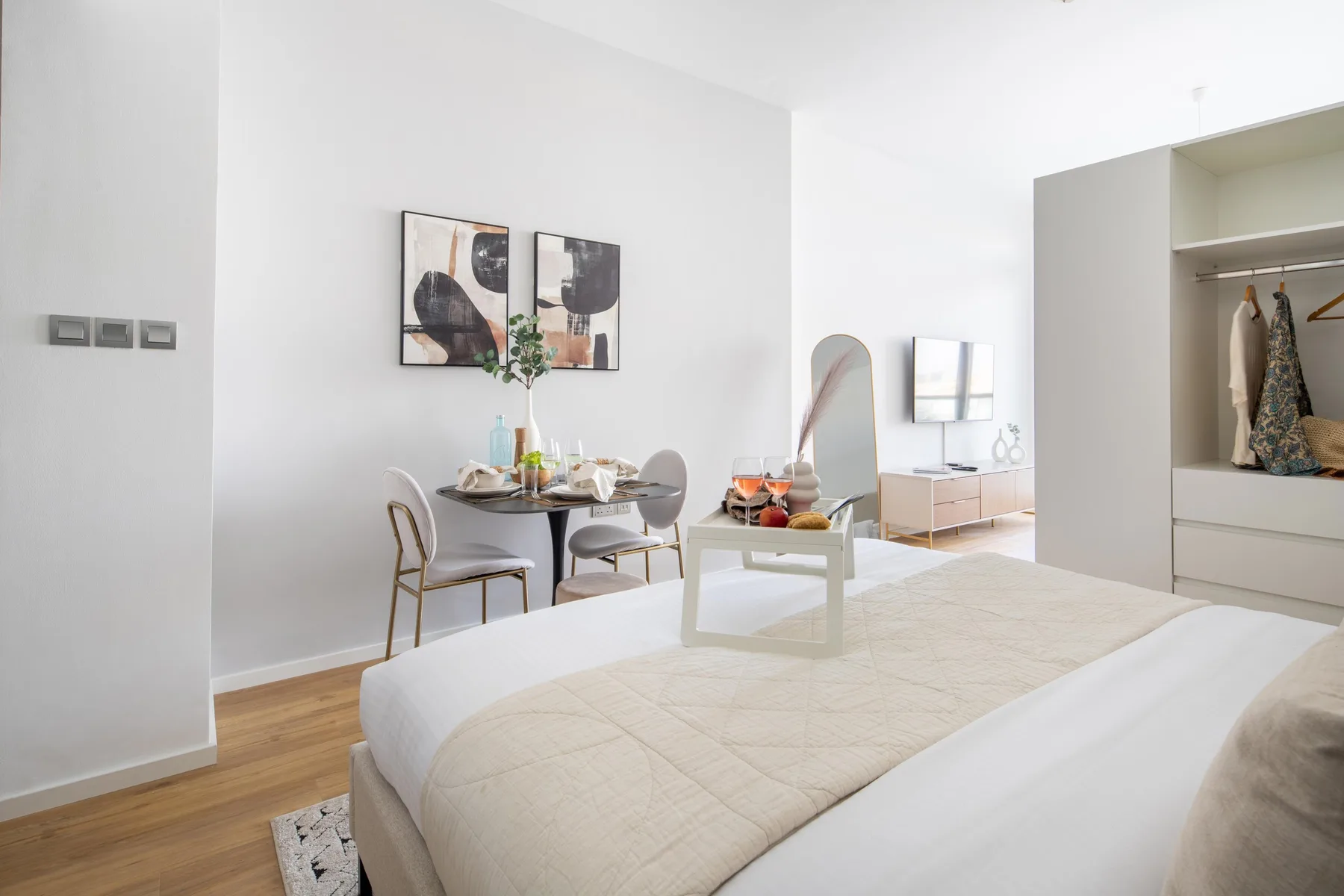 A bright bedroom with a bed, dining table, and open wardrobe.