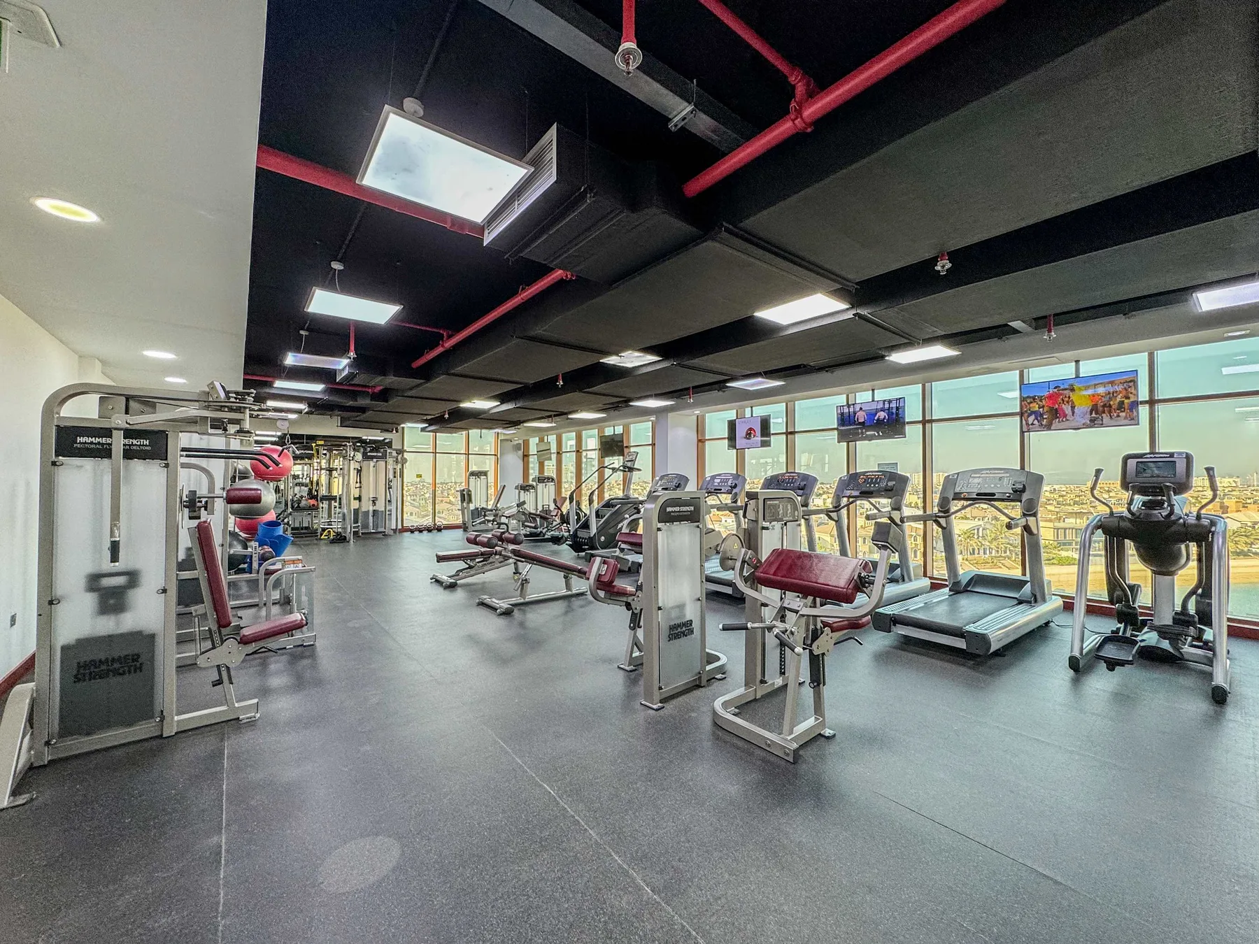 A gym with rows of exercise machines beside large windows.