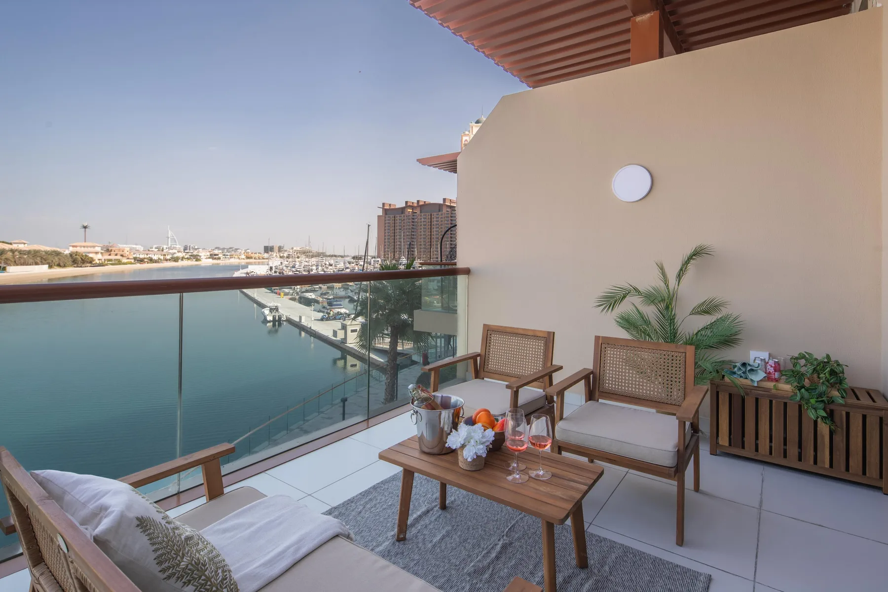A waterfront balcony seating area overlooks a marina, with plants beside the chairs.