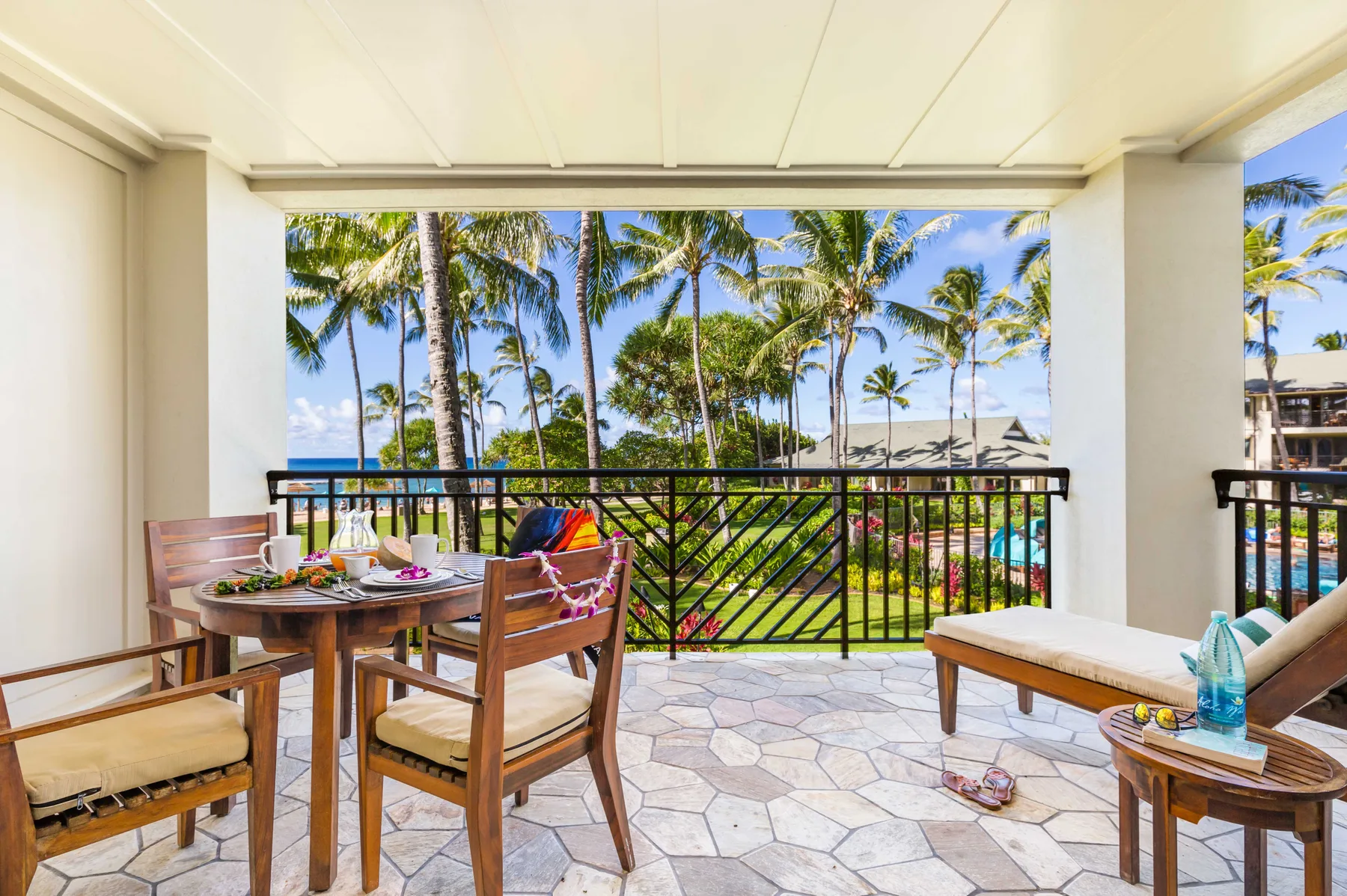 A covered patio with seating and a view of palm trees and the ocean.