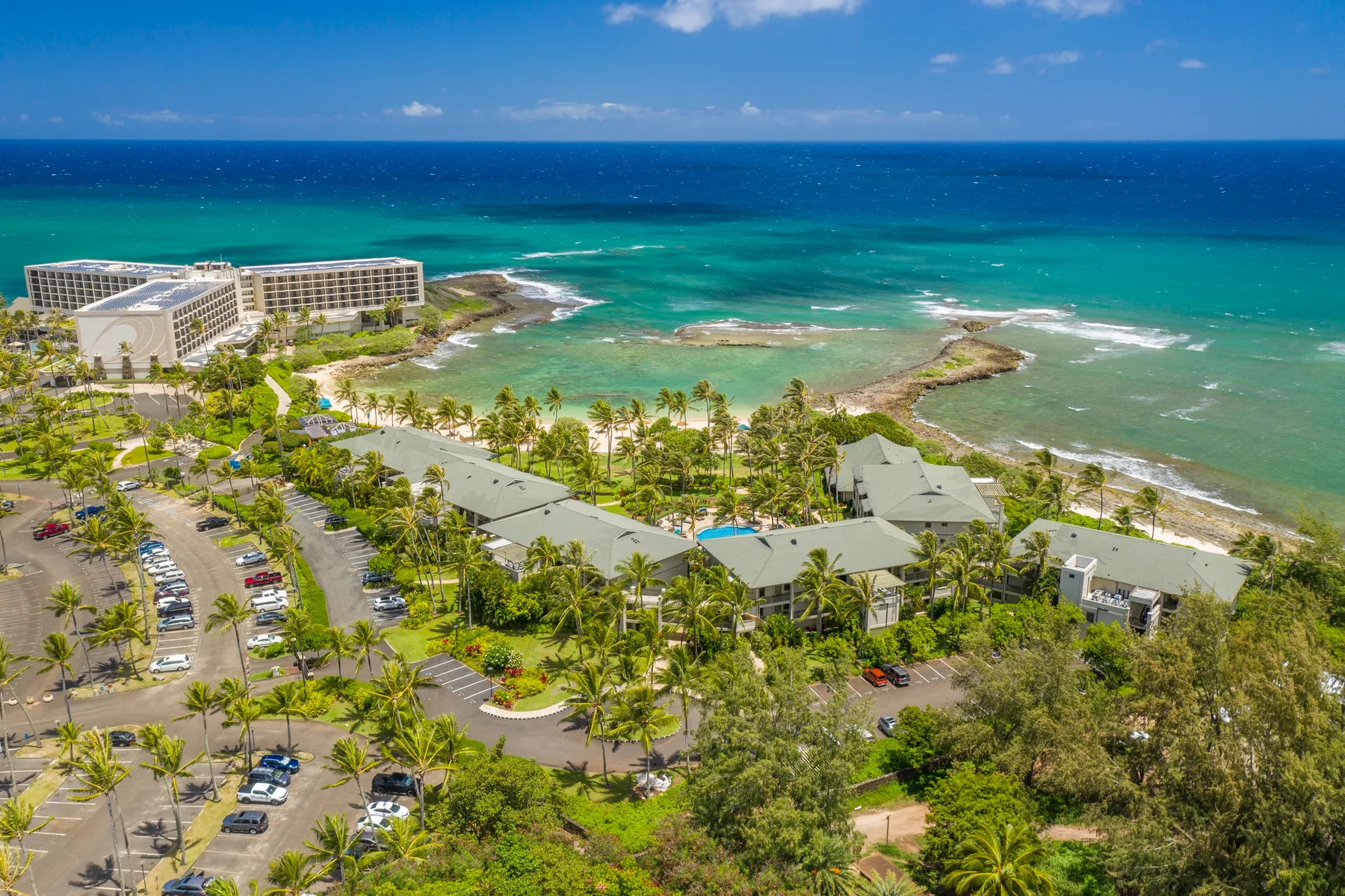 Aerial view of a tropical beachfront resort with low-rise buildings and palm trees.
