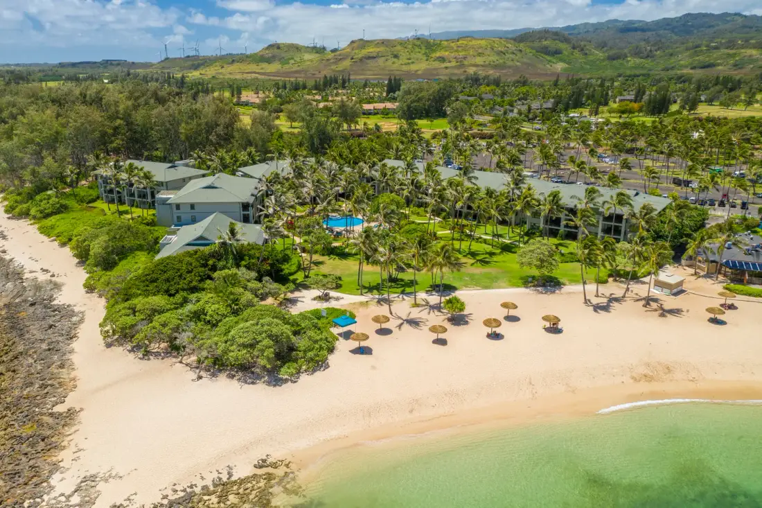 An aerial view of a beachfront resort with palm trees and a sandy shore.