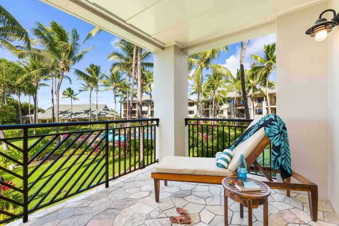A covered balcony with seating overlooks palm trees and landscaped grounds.