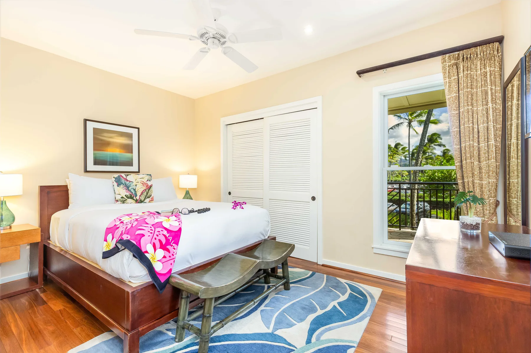 A bright bedroom with a bed, white closet doors, and a window overlooking palm trees.