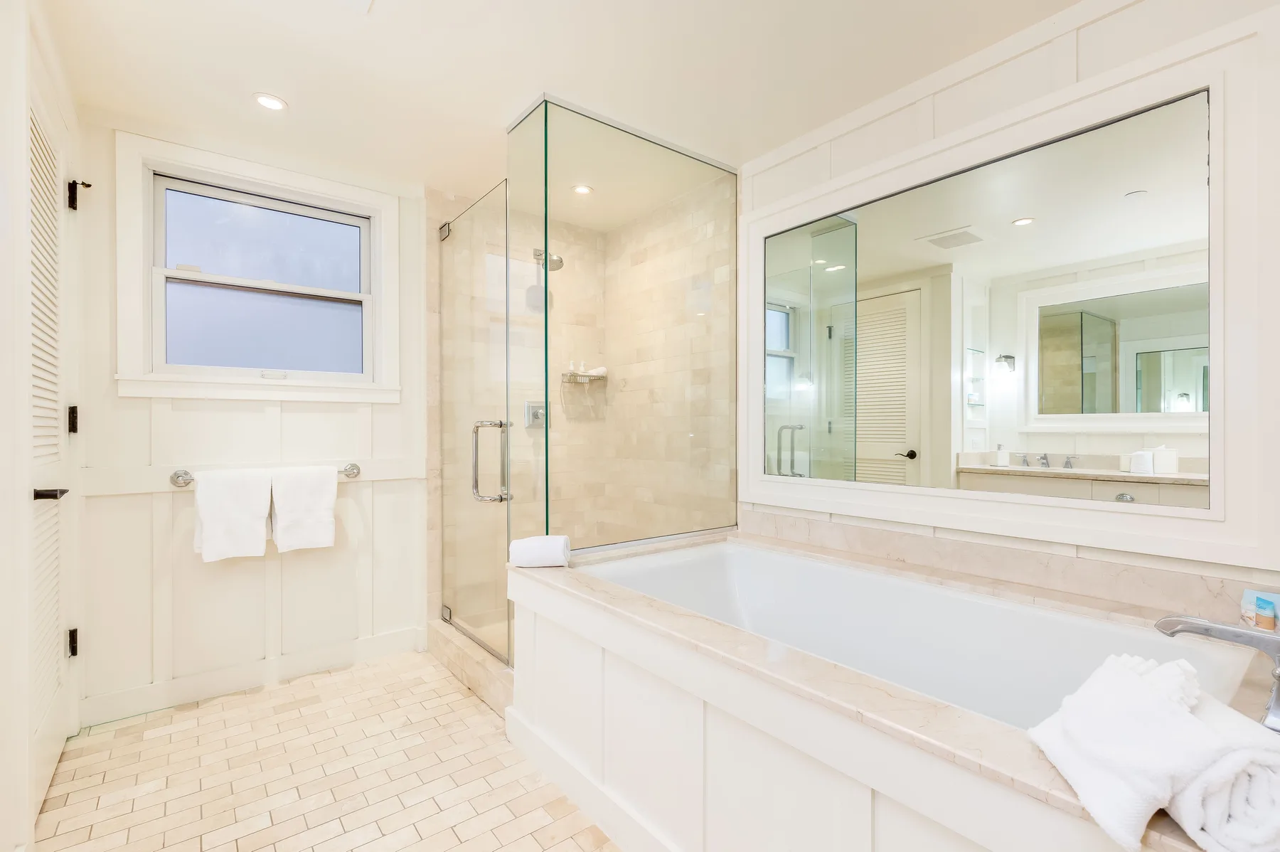 A bright bathroom with a bathtub, glass shower, and large mirror.