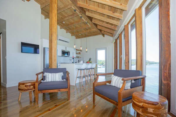 A bright open-plan living area with seating, a kitchen counter, and large windows.