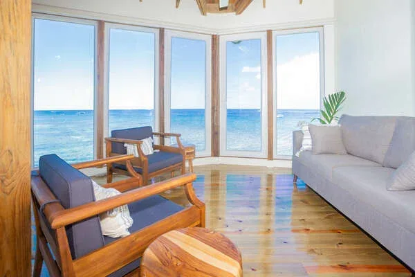 A bright living room with seating arranged beside large windows overlooking the ocean.