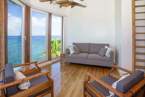 A bright living room with seating beside large windows overlooking the ocean.