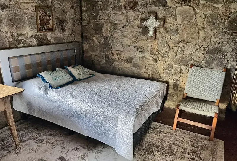 Un dormitorio con una cama y una silla junto a paredes de piedra.