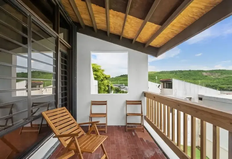 A covered balcony with wooden seating and views of green hills.