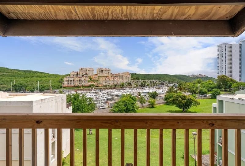 Despierta con esta impresionante vista desde tu balcón, que muestra una extensa marina rodeada de exuberantes colinas verdes y arquitectura moderna.