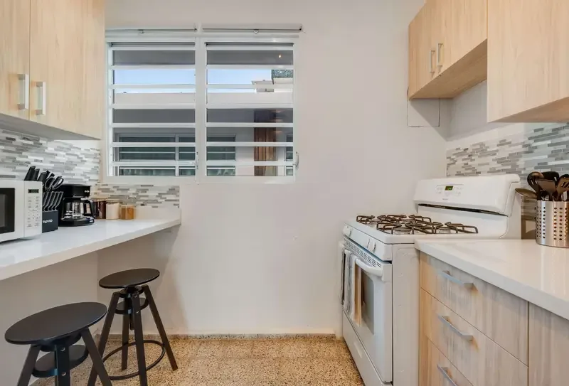 Una cocina de distribución alargada con estufa de gas, horno, refrigerador y gabinetes de madera clara.