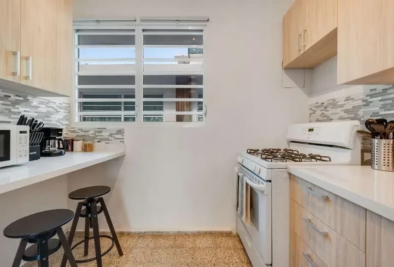 Una cocina de distribución alargada con estufa de gas, horno, refrigerador y gabinetes de madera clara.
