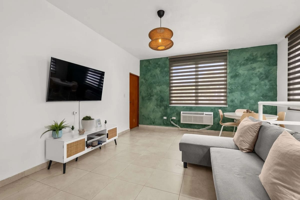 Living room with wall-mounted flat-screen TV, sofa and dining area.