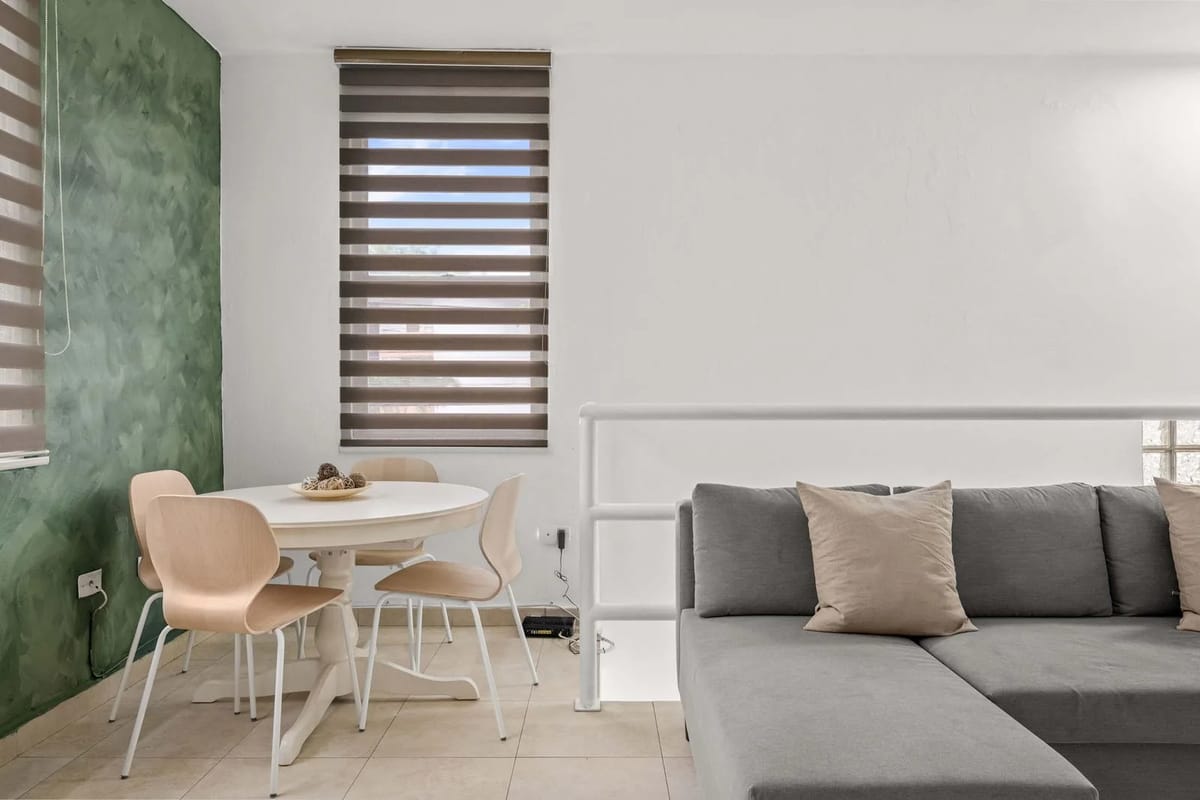 Open-concept living area with sectional sofa, dining table, windows and air-conditioning unit.