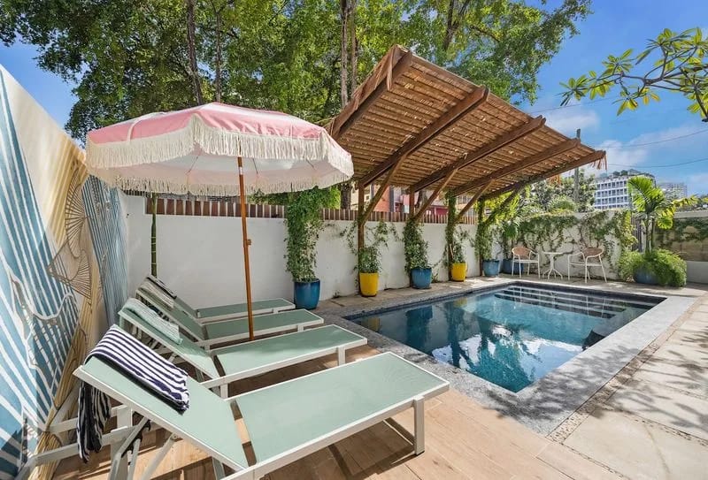 Relájese en la piscina compartida, rodeada de plantas tropicales, una pérgola de madera, tumbonas y una sombrilla.