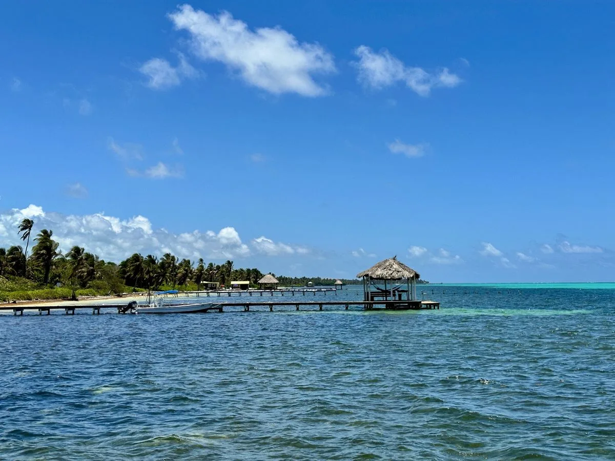 A tropical shoreline and long pier extend over clear blue water beneath a bright sky.