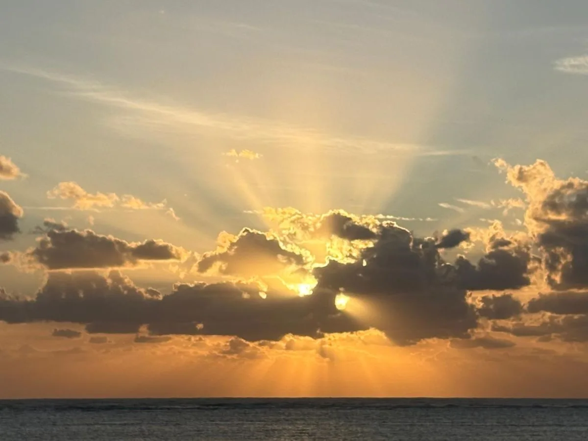 A glowing sunset shines through clouds over the ocean.