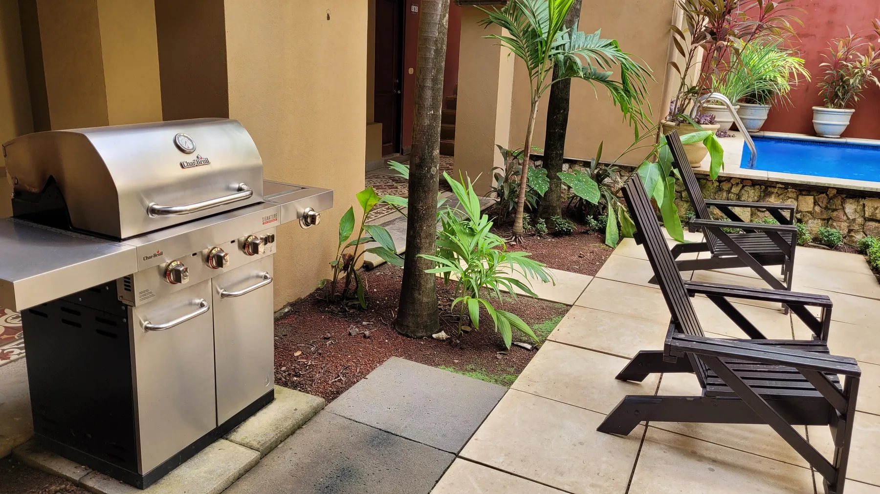 A patio with a stainless-steel grill and lounge seating beside a planted garden.