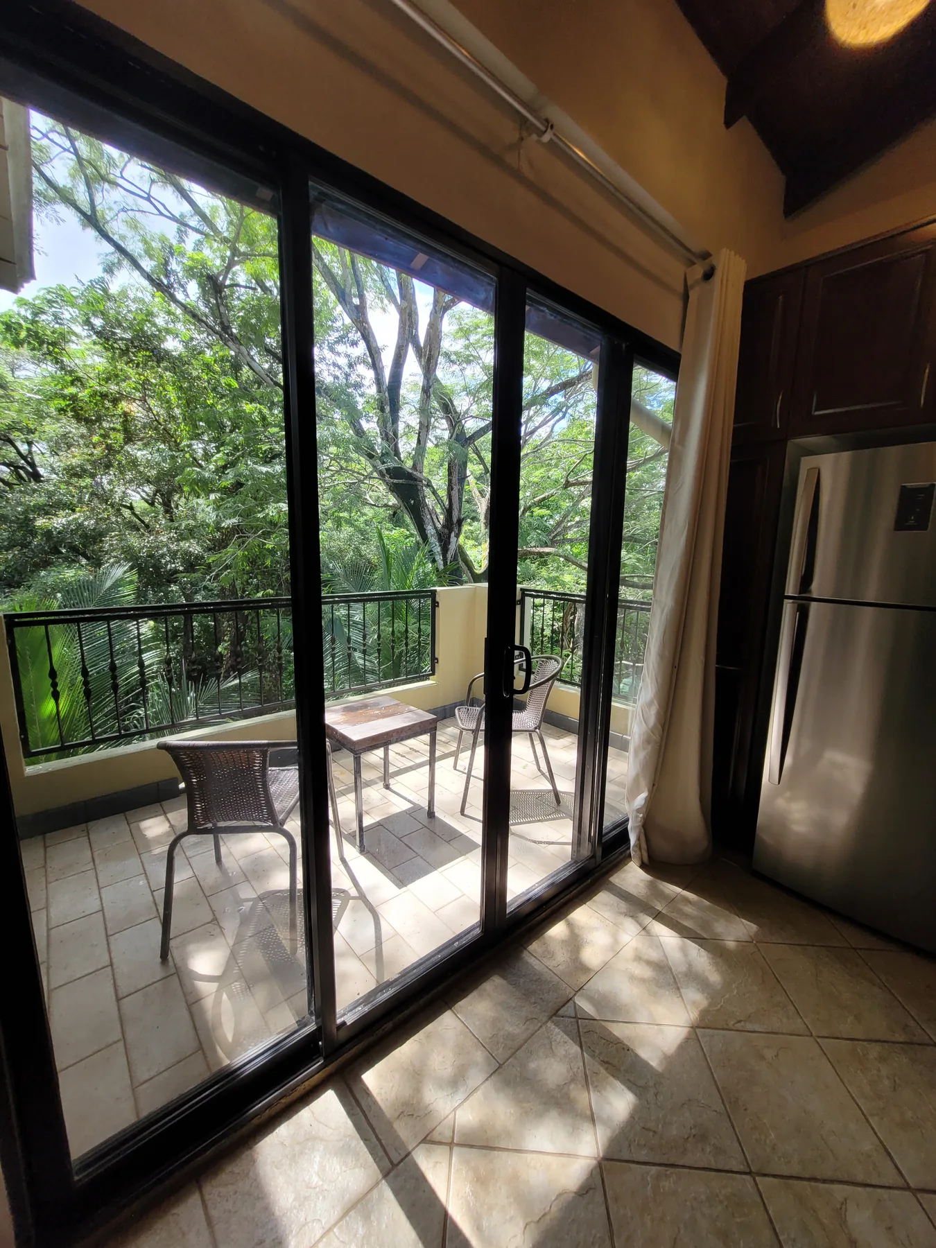 A tiled dining area opens through sliding glass doors to a balcony surrounded by trees.
